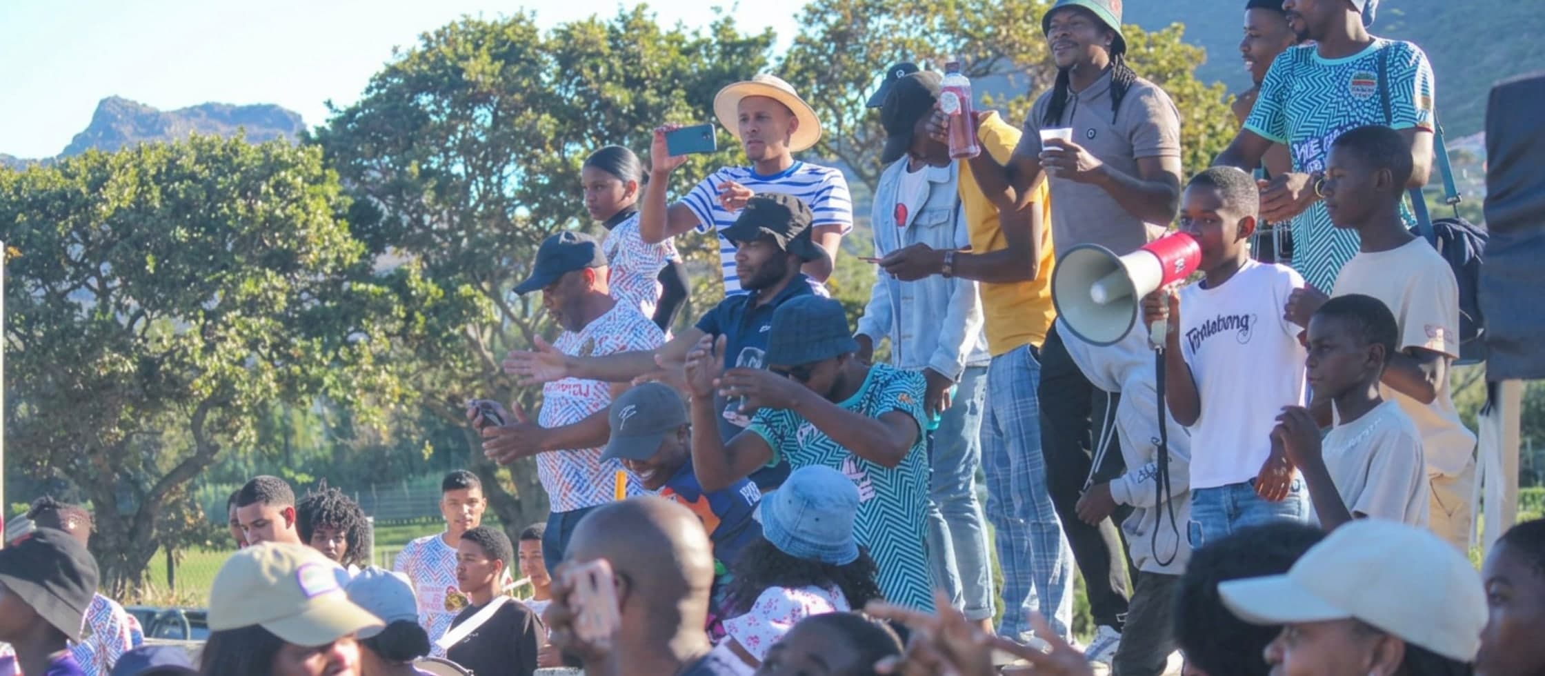 Hout Bay United supporters cheering from the stands, one leading chants with a megaphone